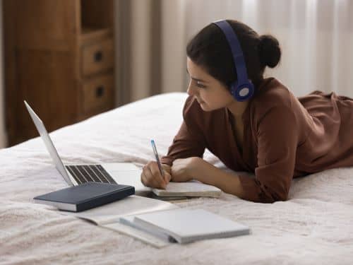 Een vrouw werkt in bed met een laptop en koptelefoon moeilijkste taal om te leren Skrivanek vertaalbureau Antwerpen