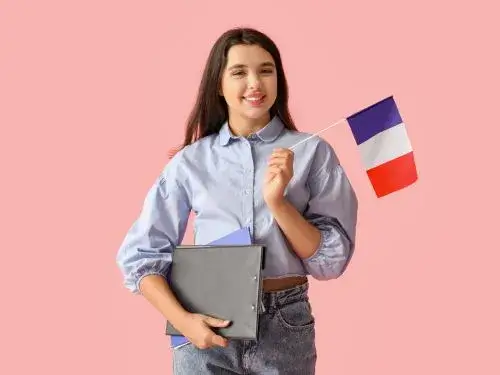 Jeune femme souriante tenant un drapeau français et des dossiers, sur fond rose le mot le plus long en français Agence de traduction Paris Jeune femme souriante tenant un drapeau français et des dossiers sur fond rose le mot le plus long en français Agence de traduction Paris